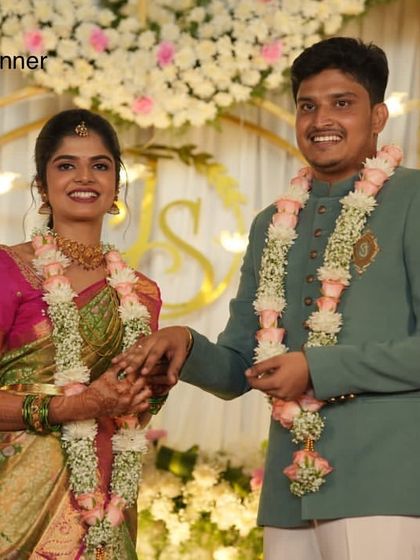 An engagement ceremony with a backdrop of white flowers and a custom monogram. The couple is framed by elegant floral garlands, adding a personal touch to their special day.