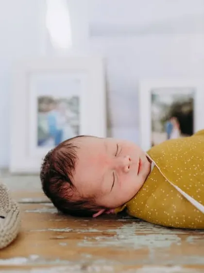 A sleeping newborn photographed next to a pair of cute knitted booties. We often use simple props to add a touch of sweetness to our baby photos.