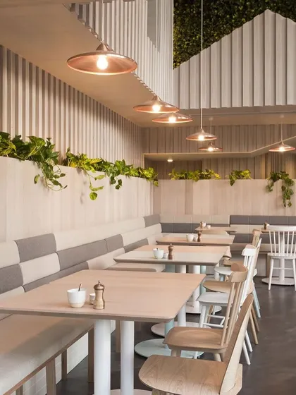 This cafe interior showcases a clean, minimalist aesthetic with a focus on natural light and textures. We used light wood for the paneling and tables, paired with custom two-tone upholstered bench seating and simple chairs to create a calm, relaxing environment perfect for a quiet coffee or meeting.