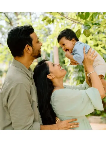 A beautiful, candid moment between parents and their child. The mother lifts the baby high, and the love and adoration are clear on everyone's faces.