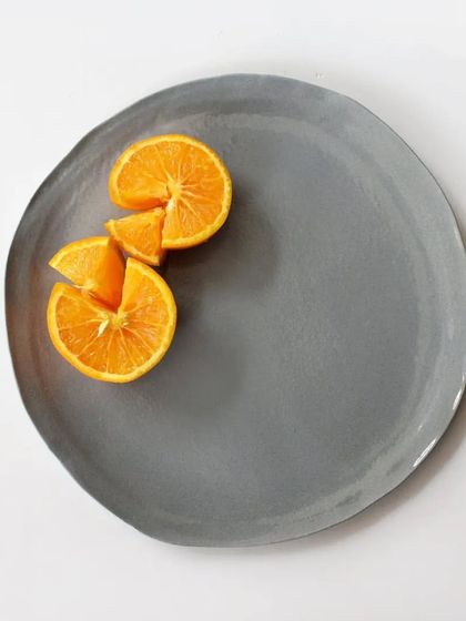 Our large monochrome grey dinner plate, shown here with fresh orange slices. The plate's organic, slightly irregular shape adds to its handmade charm and minimalist appeal.