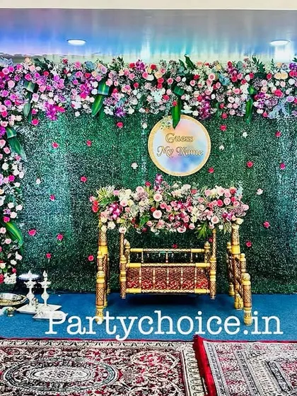 An elegant naming ceremony setup featuring a lush green floral wall as the backdrop. The cradle is adorned with matching flowers, creating a fresh and vibrant look.