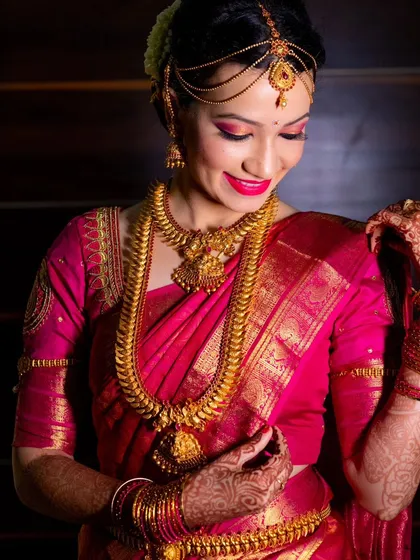A detailed shot of a bride in her gorgeous pink silk saree, admiring her intricate gold jewelry. We pay attention to every detail.