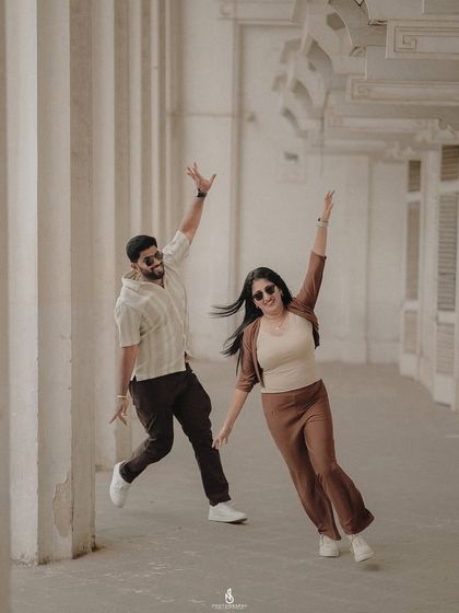 A fun, high-energy pose in a corridor with classic architectural columns. Their coordinated brown and beige outfits are stylish and modern.