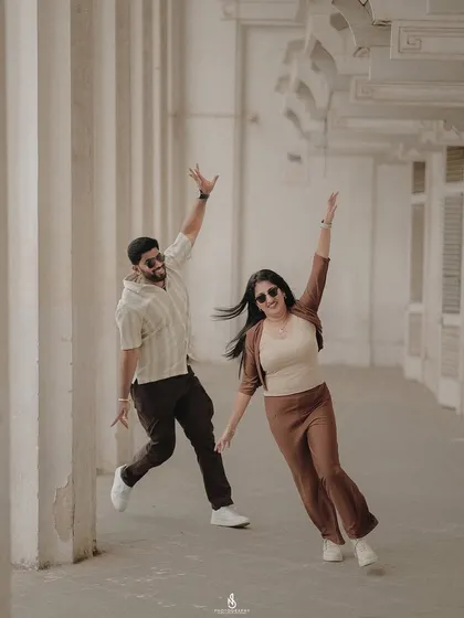 A fun, high-energy pose in a corridor with classic architectural columns. Their coordinated brown and beige outfits are stylish and modern.