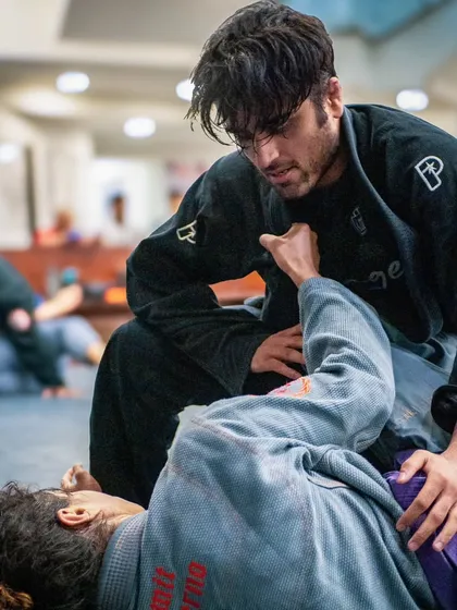 A student works to pass the guard of their training partner in a Gi. Our beginner classes focus on fundamental positions like this, building a strong base for your entire jiu-jitsu journey.