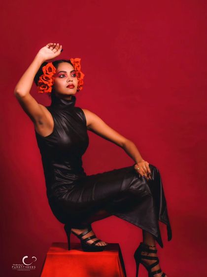 A relaxed yet powerful pose. The contrast between the black leather, red flowers, and red background is visually stunning.