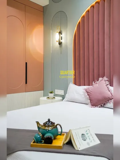 A close-up of the daughter's bedroom, showing the custom wardrobe with its curved door design and the elegant wall sconce. The combination of dusty rose, grey, and white creates a sophisticated yet youthful palette.