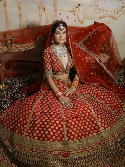 A magnificent full-length view of the bride in her elaborate red lehenga. The makeup and hair are styled to complement the grandeur of the outfit, creating a complete, breathtaking bridal vision.