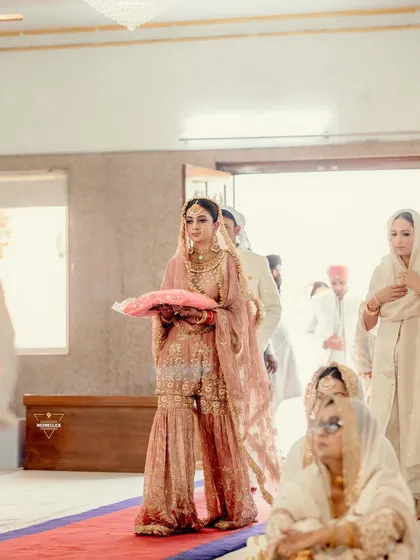 The bride's graceful entry into the Gurudwara, holding a pillow for the ceremony, a moment of tradition and reverence.