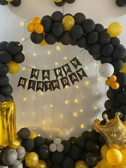 A classic black and yellow theme for a first birthday. This circular balloon arch is accented with a 'Happy Birthday' banner and a large gold crown foil balloon.