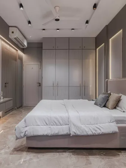This bedroom design embodies minimalism and functionality with its muted grey palette and sleek built-in wardrobes that highlight clean lines and symmetry. The floating console and layered textures add subtle elegance while maximizing space efficiency.