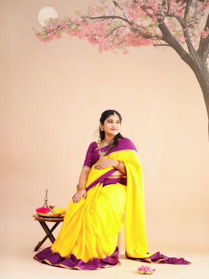 A serene portrait of an expecting mother in a yellow and purple saree, seated in a beautifully painted studio setting with a tree and moon.