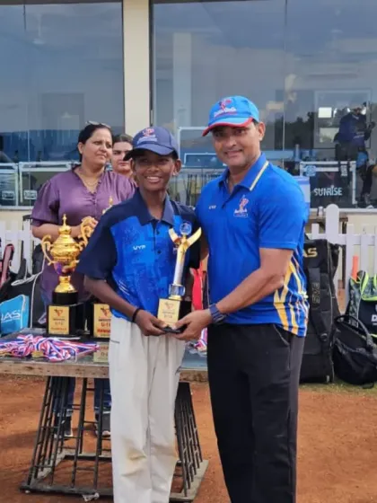A coach presents an award to a smiling player, with the main championship trophies visible on the presentation table.
