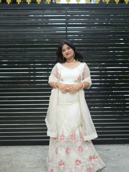 An elegant white lehenga with pink floral details, worn by a happy client. Perfect for daytime events.