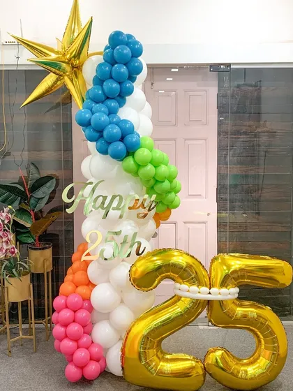 A vibrant and colorful column celebrating a 25th birthday. The rainbow spiral of balloons climbing the pillar, topped with a golden star, makes for a joyful and eye-catching party decoration.