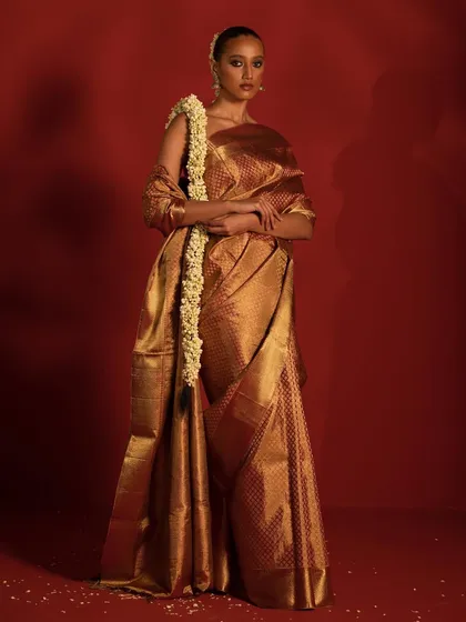 A full-length shot of a model in a magnificent golden Kanchipuram saree, styled with a trail of jasmine flowers in her hair for a traditional yet dramatic effect.