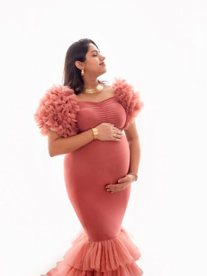 A serene solo portrait of a mom-to-be in a dusty rose mermaid gown, basking in the soft light against a clean white background.