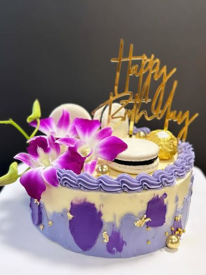 A beautiful purple watercolor cake decorated with fresh orchids, macarons, and Ferrero Rocher. The gold details make it extra special.