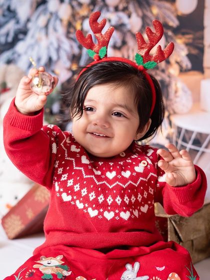 A baby in a festive red sweater with reindeer antlers. The holiday props and outfits add to the charm of these annual photoshoots.