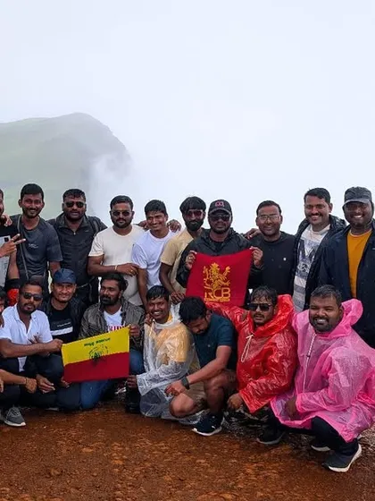 A large group celebrating their achievement at the peak, proudly holding the Karnataka flag.