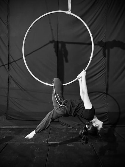 A graceful backbend pose on the bottom of the hoop, captured in a dramatic black and white photo.