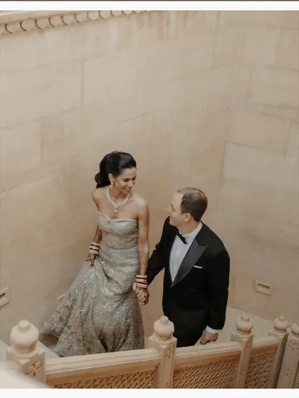 Ascending the stone staircase at Suryagarh, hand in hand. This shot captures a sense of journey and partnership, their elegant evening wear contrasting with the ancient, textured walls of the fortress.