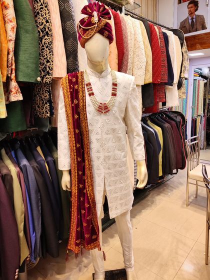 This exclusive white sherwani is designed for the 2024 wedding season. It features intricate cutwork and is styled with a maroon velvet stole and a matching turban for a regal finish.