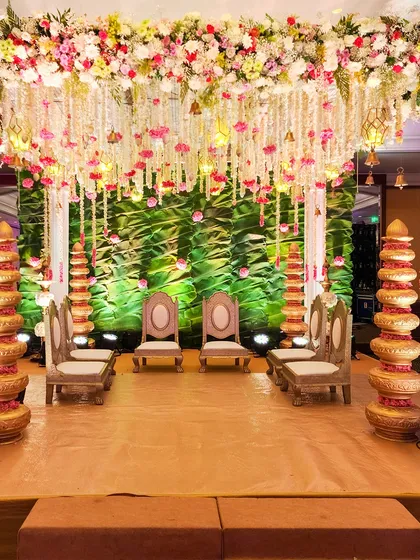 We designed this indoor mandap with a lush green backdrop to contrast with the hanging floral strings of jasmine and pink roses, creating a vibrant and fresh look.