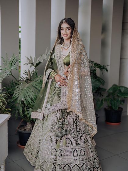 A bride looking radiant in our olive green lehenga. The intricate silver and white embroidery stands out beautifully against the deep green fabric, offering a unique and elegant choice for a wedding or reception.