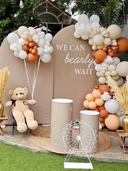 The "We can bearly wait" theme is perfect for a sweet and modern baby shower. This outdoor setup features a neutral color palette with beige, brown, and white balloons, pampas grass, and a cute teddy bear holding his own balloon bouquet.