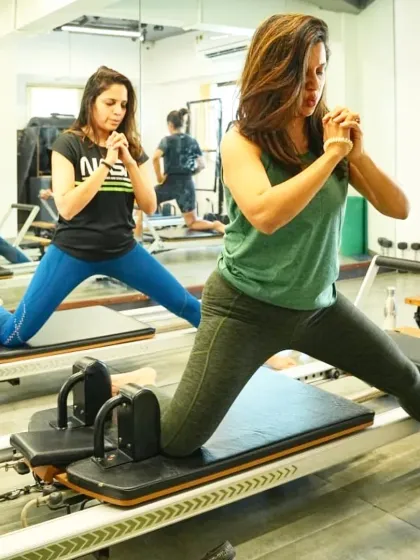 Two clients work in sync on their reformers, motivating each other through their workout. A consistent routine helps boost energy, build strength, and create a healthier mind and body.