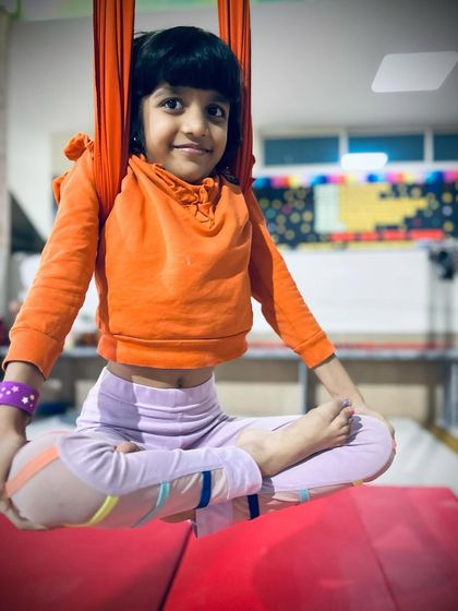 A young student finds her center, sitting in a perfect lotus pose while suspended in the aerial hammock.