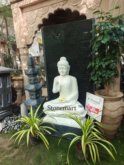 A full view of the 5-foot Blessing Buddha fountain, showing how it commands presence in a garden setting. The contrast between the white marble statue and the dark granite waterfall makes it a striking visual anchor.