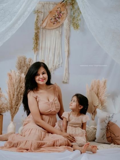 A mother and daughter sit together in a beautifully styled bohemian studio setup. The daughter looks up at her mother, creating a sweet and storytelling moment.