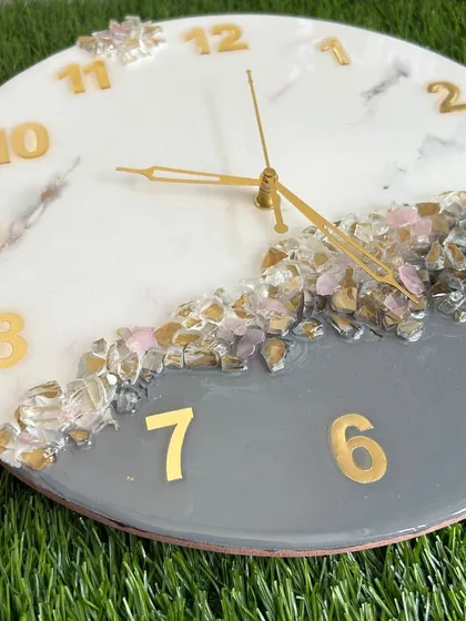 This clock features a unique design with grey, white, and pinkish tones, accented with delicate pink and gold crystals.