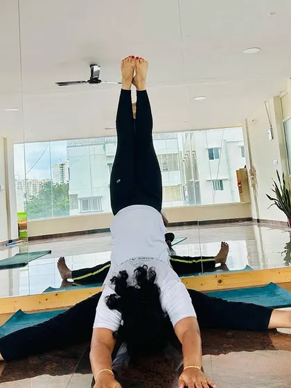 A creative partner pose combining a supported headstand with a wide-legged forward fold. This demonstrates the trust, balance, and strength shared between our students.