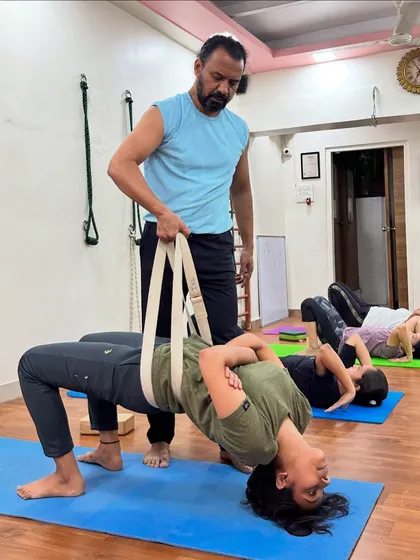 I am guiding a student through Grivasana, or the Neck Pose, using a yoga belt for support. This advanced posture is excellent for strengthening the neck and pelvic floor muscles and can also help in managing thyroid-related issues.