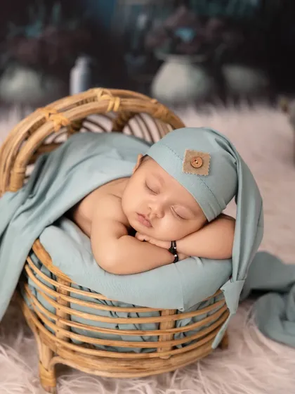 This newborn sleeps peacefully in a miniature rattan bed. The teal-colored swaddle and hat create a beautiful color harmony with the rustic and natural props.