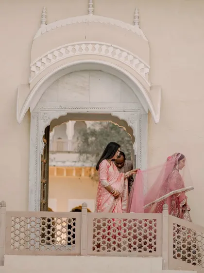 A candid moment of the bride on a palace balcony, her veil being adjusted before the ceremony, capturing the quiet moments of preparation.