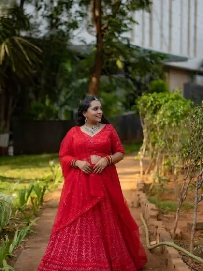A full-length shot of the red lehenga in a garden setting, showing its vibrant color and flow.