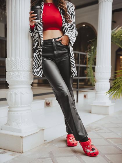 A stylish on-location shoot for Crocs. The model's confident pose against the white pillars, combined with the zebra-print blazer and red Crocs, creates a bold, fashion-forward look.