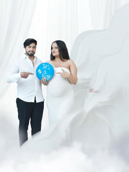 A fun gender reveal photo with an expecting couple. They point to a blue balloon that says "It's a Boy," sharing their exciting news in a beautiful studio setting.