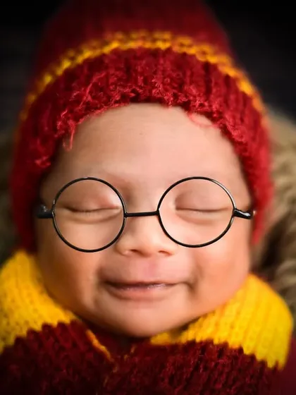 A close-up of a smiling newborn dressed as Harry Potter. Even in their sleep, their personality can shine through.