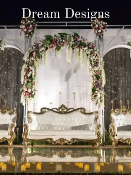 A detailed shot of the central part of the reception stage. The ornate white and gold furniture sits before a backdrop of shimmering lights and floral arches, creating a regal focal point.