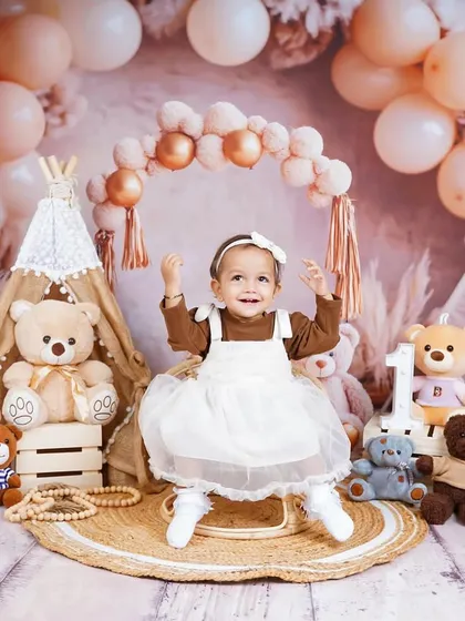A boho-chic first birthday theme with pampas grass, balloons, and teddy bears. This little one's joyful expression is infectious.