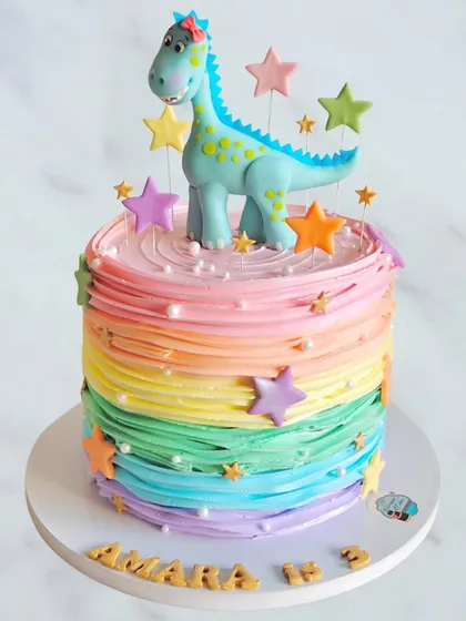 A vibrant rainbow-striped dinosaur cake. This colorful whipped cream design combines a playful dinosaur topper with a multi-hued frosting technique, perfect for a cheerful birthday celebration.