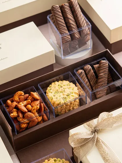A sleek, modern gift box with three compartments holding roasted nuts, a pistachio cookie, and chocolate-drizzled sticks. This is a perfect example of my elegant and minimalist corporate gifting options.