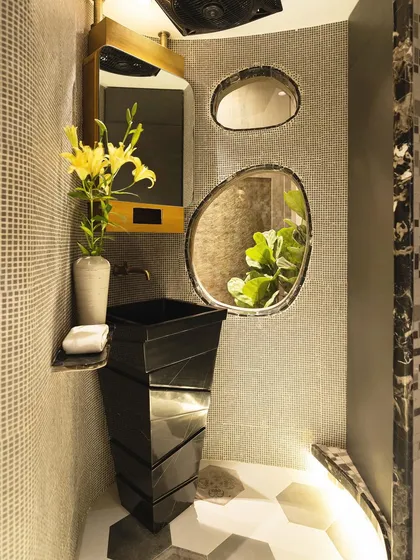 The bathroom is a study in luxury, with a black marble pedestal sink and curved walls adorned with mosaic tiles. The design uses organic shapes and high-contrast materials for a dramatic effect.