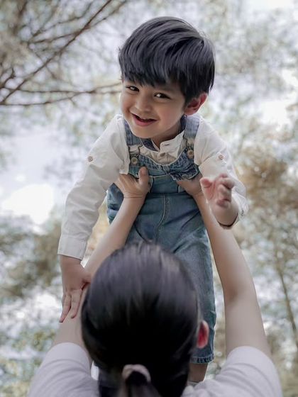 A mother lifts her smiling son up, captured from a low angle to emphasize the joy of the moment.